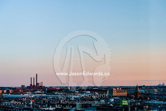 Factory chimneys rise above the flat city skyline of Copenhagen at sunset. Copenhagen, Denmark.