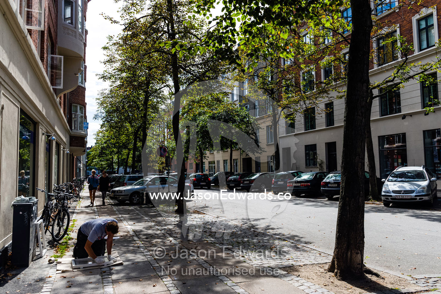 A person sanding paint from a window frame on the footpath. Copenhagen, Denmark.