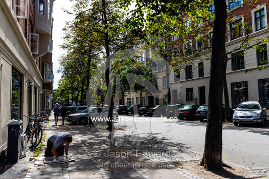 A person sanding paint from a window frame on the footpath. Copenhagen, Denmark.