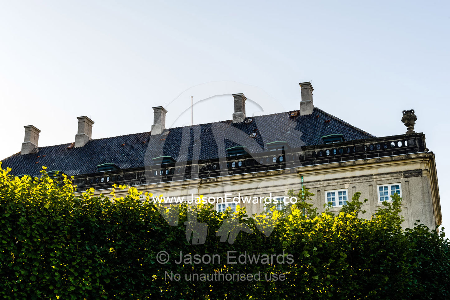 The roofline of the Royal Palace rises over a hedge wall. Amalienborg Palace, Copenhagen, Denmark.