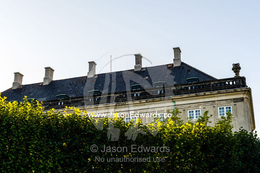 The roofline of the Royal Palace rises over a hedge wall. Amalienborg Palace, Copenhagen, Denmark.