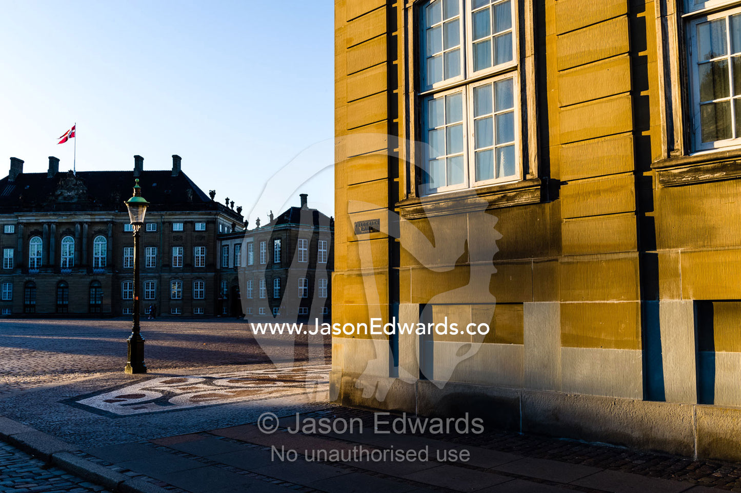 Sunset falls across the facade of the Royal Palace and it's cobblestone courtyard. Amalienborg Palace, Copenhagen, Denmark.
