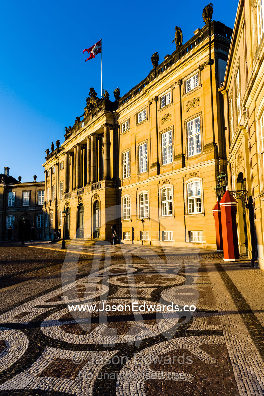 Sunset falls across the facade of the Royal Palace and it's cobblestone courtyard and guard post. Amalienborg Palace, Copenhagen, Denmark.