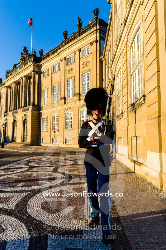 A member of the Royal Guard patrols the palace at sunset with a rifle. Amalienborg Palace, Copenhagen, Denmark.