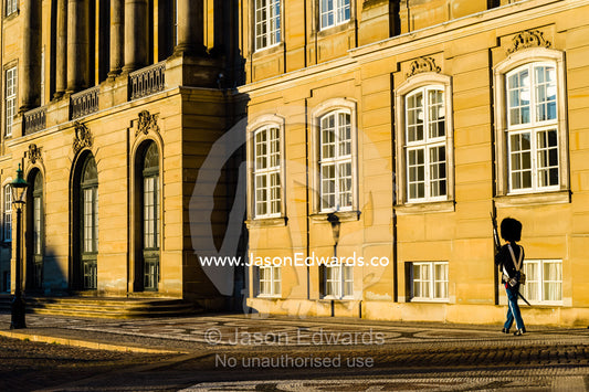 A member of the Royal Guard patrols the palace at sunset with a rifle. Amalienborg Palace, Copenhagen, Denmark.