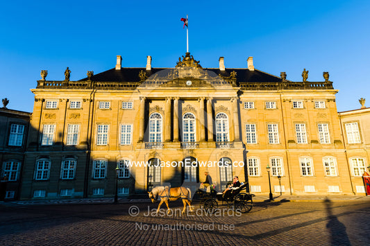 Sunset falls across the facade of the Royal Palace and a horse drawn carriage in it's cobblestone courtyard. Amalienborg Palace, Copenhagen, Denmark.