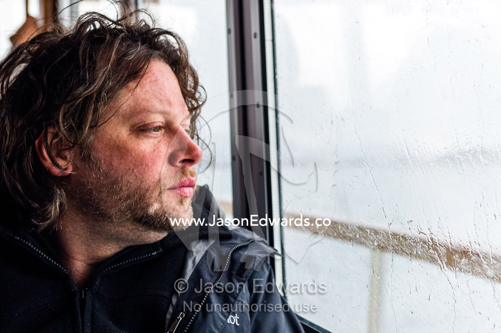 A man looks out the rain splattered window of a water taxi in the arctic. Fjord of Eternity, Maniitsoq, Sukkertoppen, Qeqqata Municipality, Greenland.