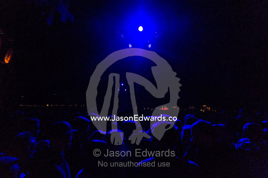 The heads of people in a crowd watching a concert illuminated by neon blue lights. Tivoli Gardens, Copenhagen, Denmark.