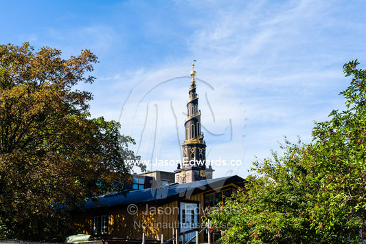 The spiral spire of the Church of Our Saviour seen between trees. Christiania, Freetown Christiania, Christianshavn, Copenhagen, Denmark.