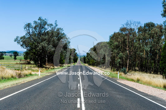 A long, straight country road passing through farmland. Peak Hill, New South Wales, Australia.