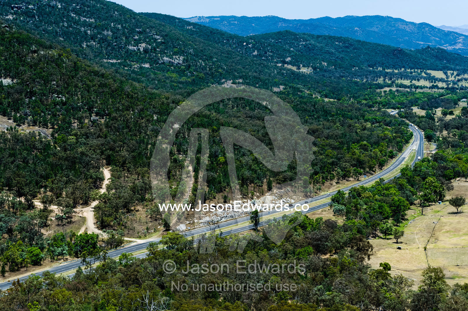 A multi-lane highway rounding the base of a mountain through farmland. Glen Innes, New South Wales, Australia.
