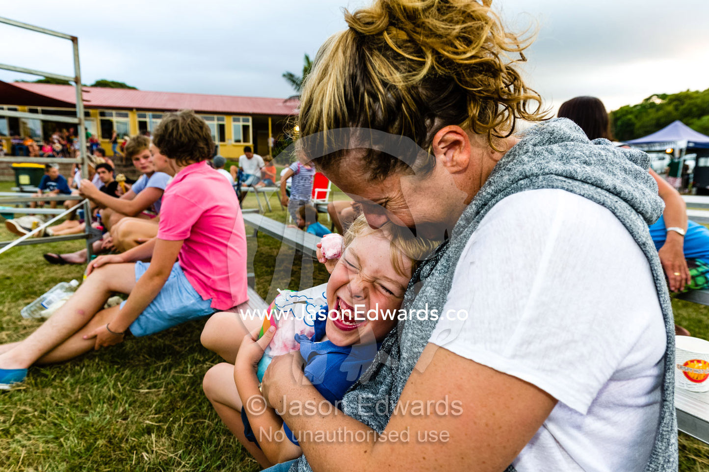 A mother tickles her laughing son at a rodeo. Byron Bay, New South Wales, Australia.