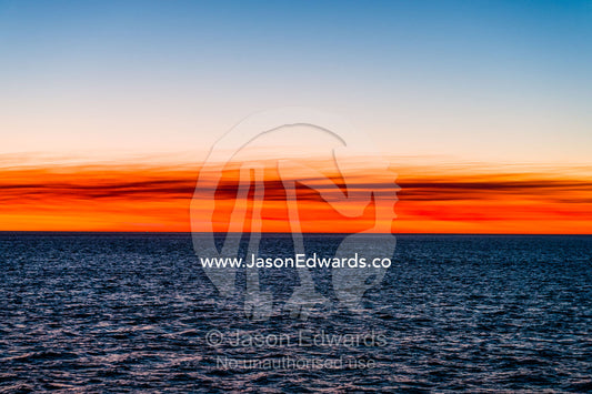 Flaming red afterglow over the ocean horizon at sunset. Broome, Kimberley Coast, Western Australia, Australia.