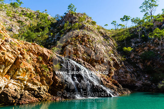 A small waterfall cascades into a sandstone gorge waterhole in the desert. Crocodile Creek, Kimberley Coast, Western Australia, Australia.