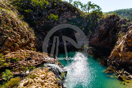 A small waterfall cascades into a sandstone gorge waterhole in the desert. Crocodile Creek, Kimberley Coast, Western Australia, Australia.