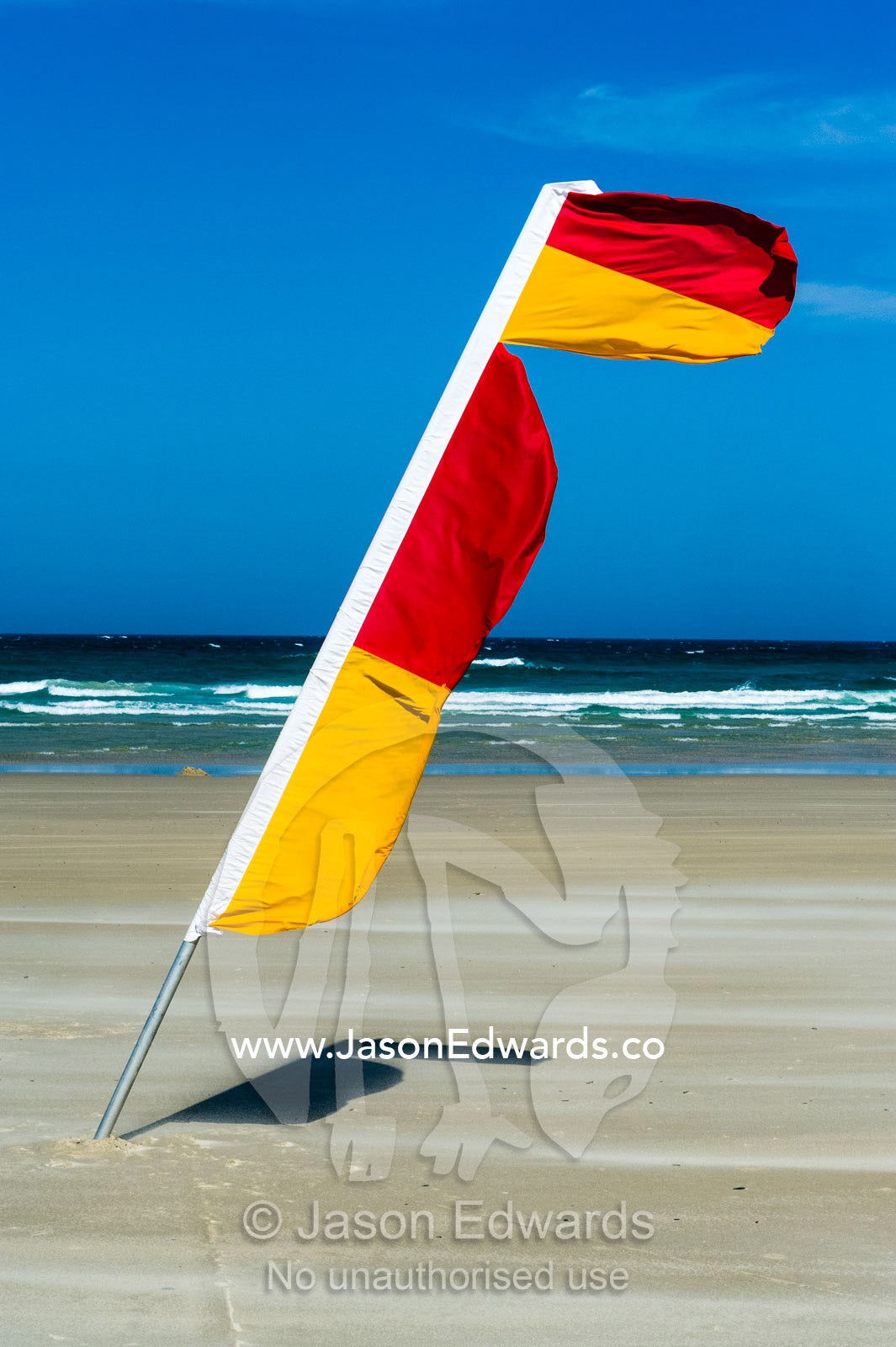 A surf lifesaving flag identifies the patrolled swimming area on a beach. Byron Bay, New South Wales, Australia.