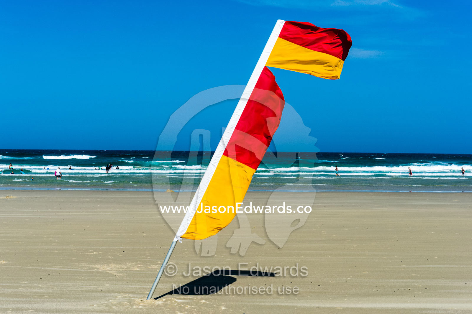 A surf lifesaving flag identifies the patrolled swimming area on a beach. Byron Bay, New South Wales, Australia.