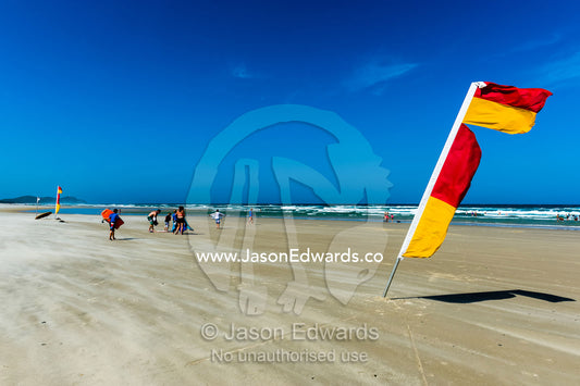 A surf lifesaving flag identifies the patrolled swimming area on a beach. Byron Bay, New South Wales, Australia.