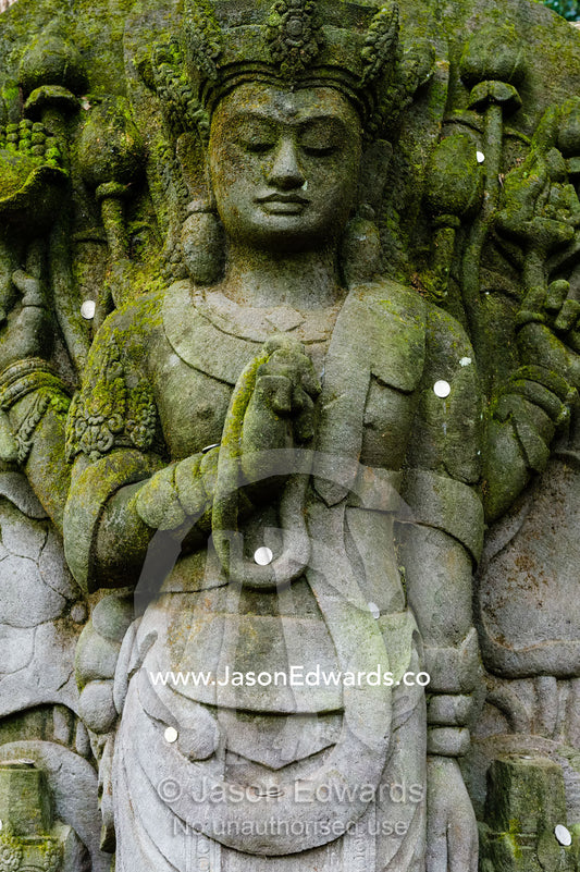 A moss covered statue of Avalokiteshvara in a botanical garden. Crystal Castle, Shambhala Gardens, Mullumbimby, New South Wales, Australia.