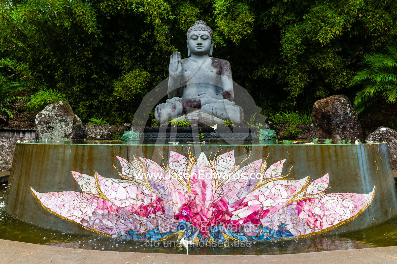 A statue of buddha offering a blessing over a lotus pond in a botanical garden. Crystal Castle, Shambhala Gardens, Mullumbimby, New South Wales, Australia.