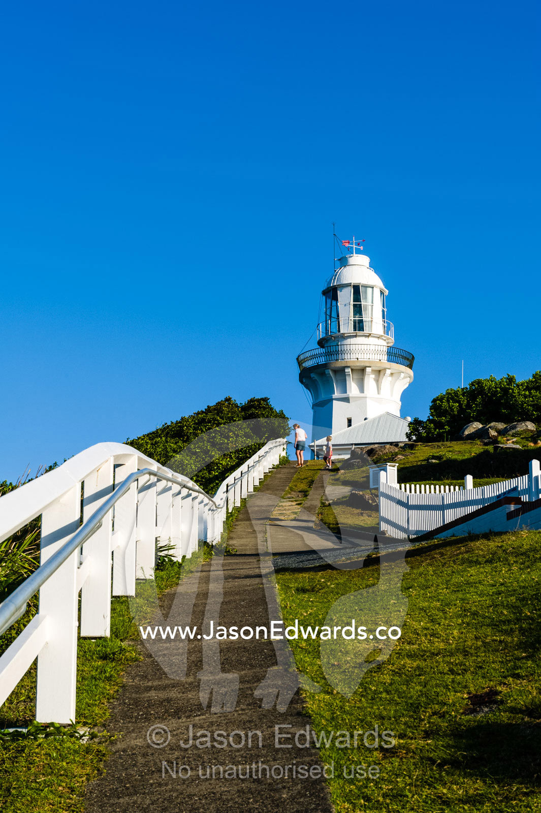 A pathway and whit picket fence leading to a lighthouse on a cliff top. Smoky Cape Lighthouse, Hat Head National Park, New South Wales, Australia.