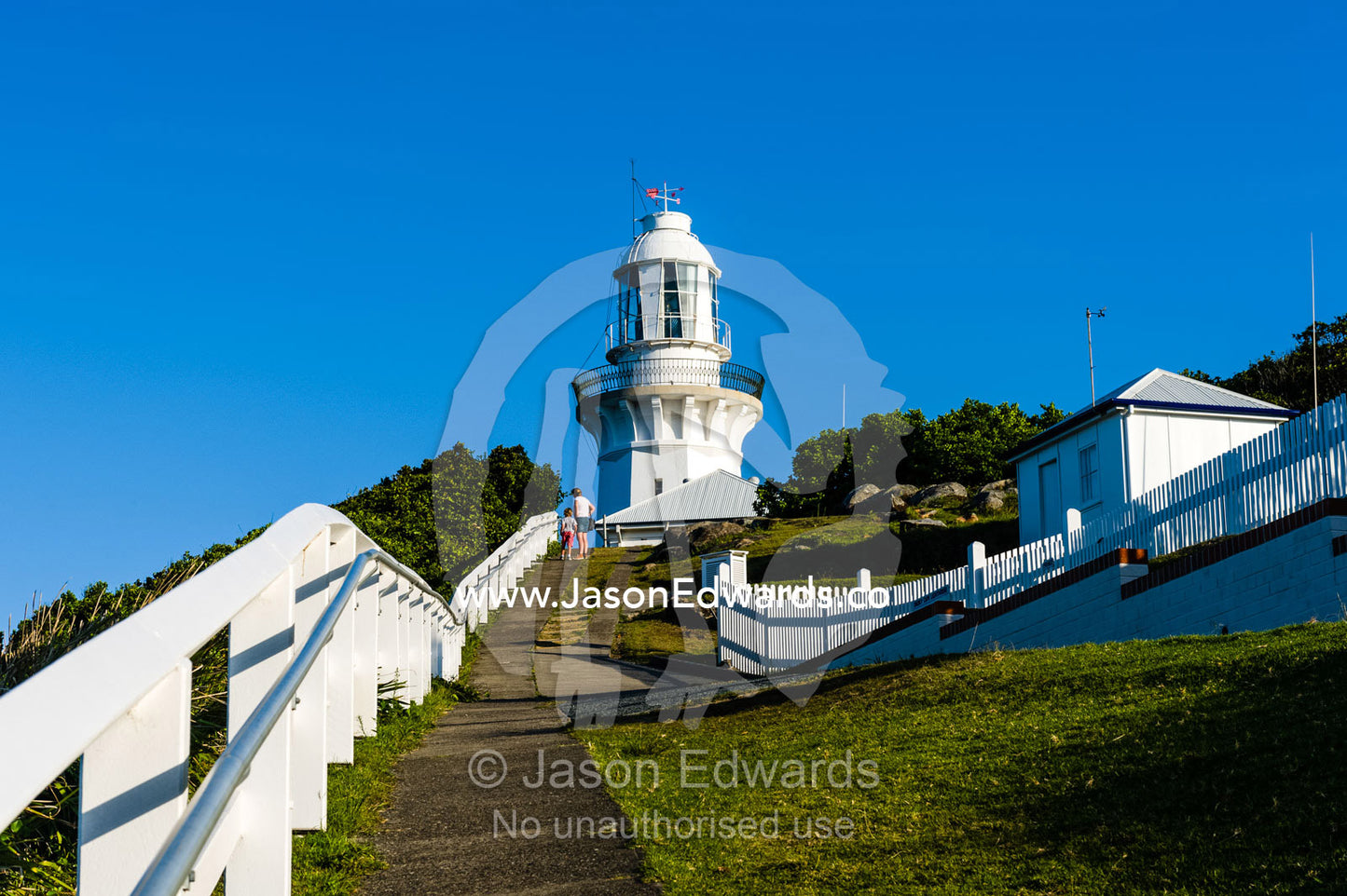 A pathway and whit picket fence leading to a lighthouse on a cliff top. Smoky Cape Lighthouse, Hat Head National Park, New South Wales, Australia.