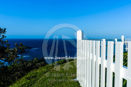 A white picket fence around a lighthouse keepers cottage overlooks the ocean. Smoky Cape Lighthouse, Hat Head National Park, New South Wales, Australia.