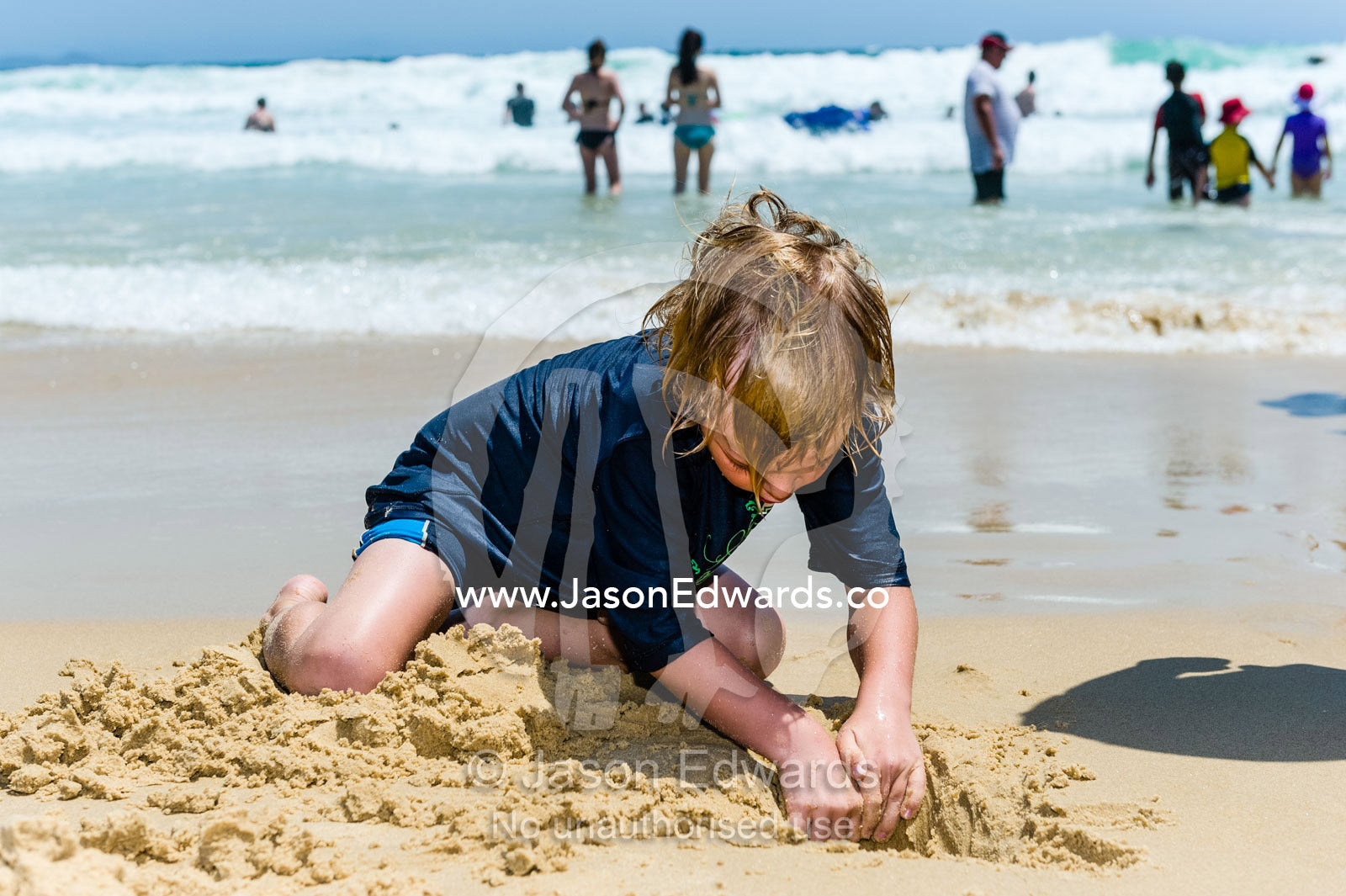 A boy digging in the sand on a beach at low tide. South West Rocks, New South Wales, Australia.