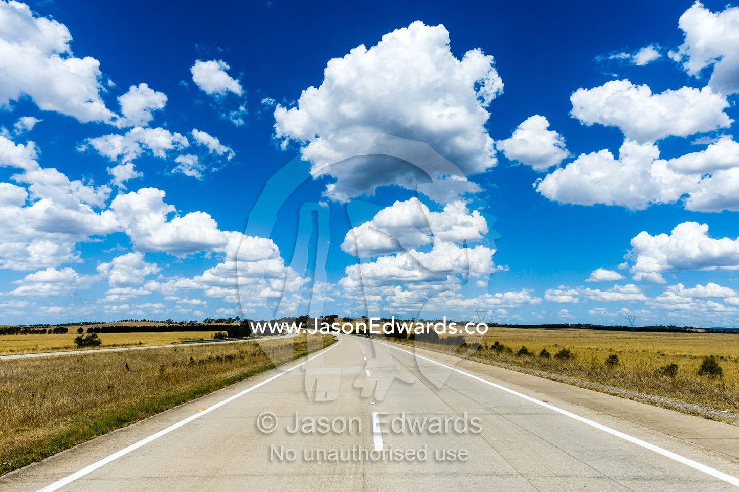 Fluffy white clouds above a highway passing through dry farmland. Holbrook, New South Wales, Australia.