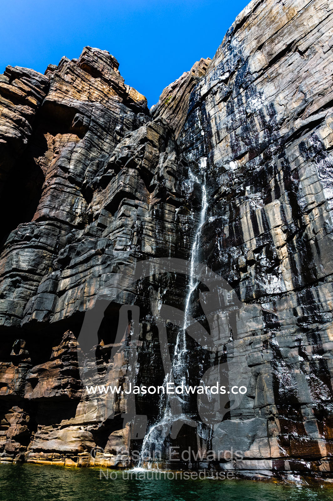 A waterfall cascades down a sheer sandstone cliff covered in cyanobacteria. King George River, King George Falls, Gardner Plateau, Kimberley Coast, Western Australia, Australia.