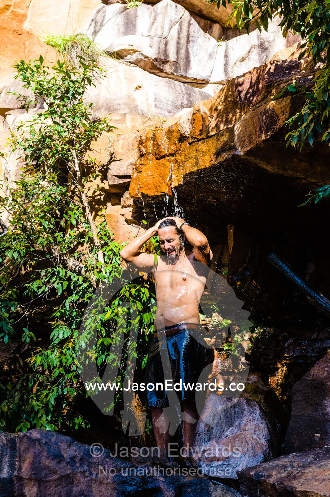 A man takes a cool shower under a small freshwater waterfall in a desert gorge. Calamity Bay, Koolama Bay, Kimberley Coast, Western Australia, Australia.