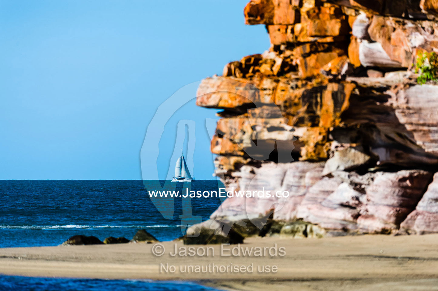 A catamaran sailing past a secluded beach on a desert coastline. Calamity Bay, Koolama Bay, Kimberley Coast, Western Australia, Australia.