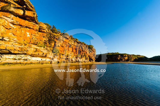 The reflection of orange ochre cliffs in a tidal pool on a beach at sunset. Calamity Bay, Koolama Bay, Kimberley Coast, Western Australia, Australia.