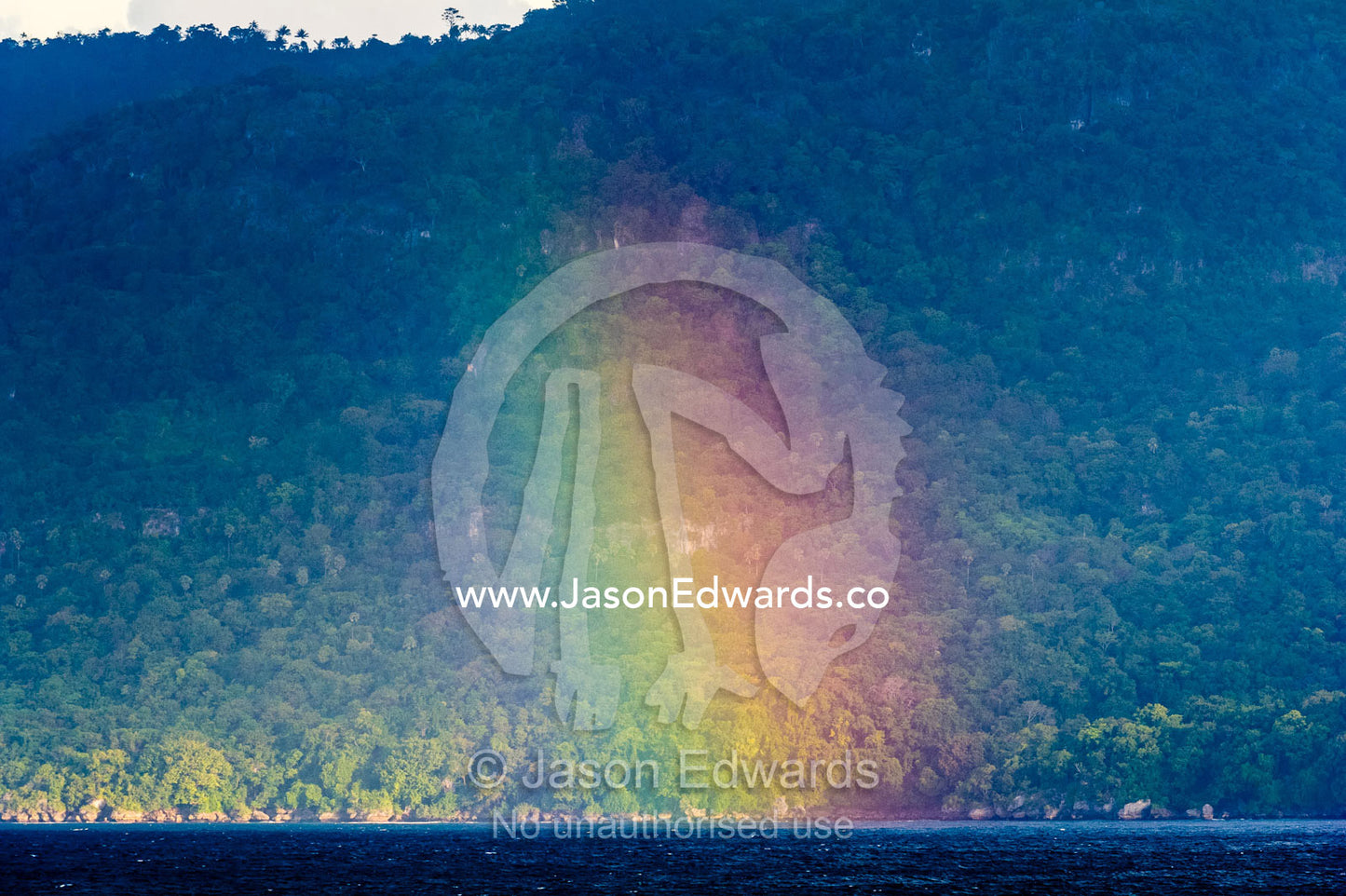A rainbow touches the ocean in front of rainforest in East Timor. Com, Sunda Islands, Timor-Leste, East Timor.