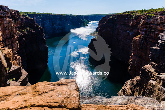 A river flowing beneath sheer ochre sandstone canyon walls on a desert coastline. King George River, King George Falls, Gardner Plateau, Kimberley Coast, Western Australia, Australia.
