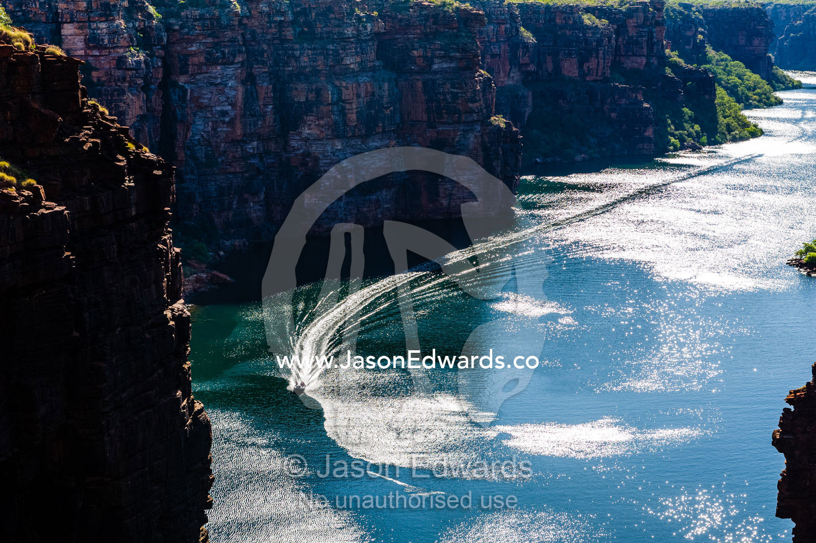 A boat cruising along a river beneath sheer cliff walls. King George River, King George Falls, Gardner Plateau, Kimberley Coast, Western Australia, Australia.