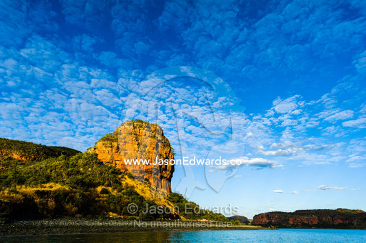 A rugged sandstone headland at the mouth of a river rises into a blue sky. Naturalists Island, Wunumpurramarra, Hunter River, Kimberley Coast, Western Australia, Australia.