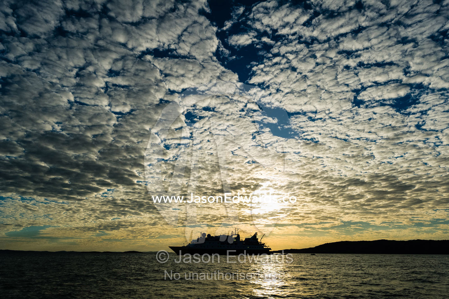 The silhouette of a cruise ship on the horizon at sunset. Naturalists Island, Wunumpurramarra, Hunter River, Kimberley Coast, Western Australia, Australia.