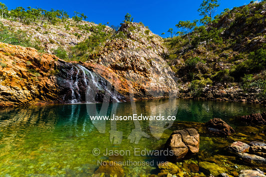 A small waterfall cascades into a sandstone gorge waterhole in the desert. Crocodile Creek, Kimberley Coast, Western Australia, Australia.
