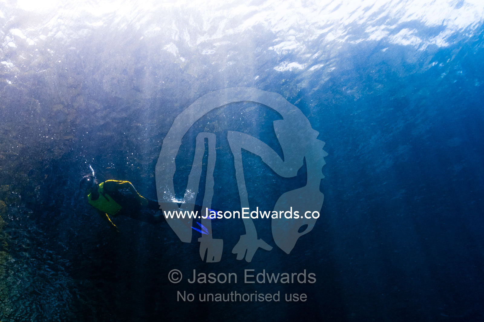 A tourist snorkeling through sunrays over a coral reef. Friwinbonda Island, Raja Ampat, Indonesia.