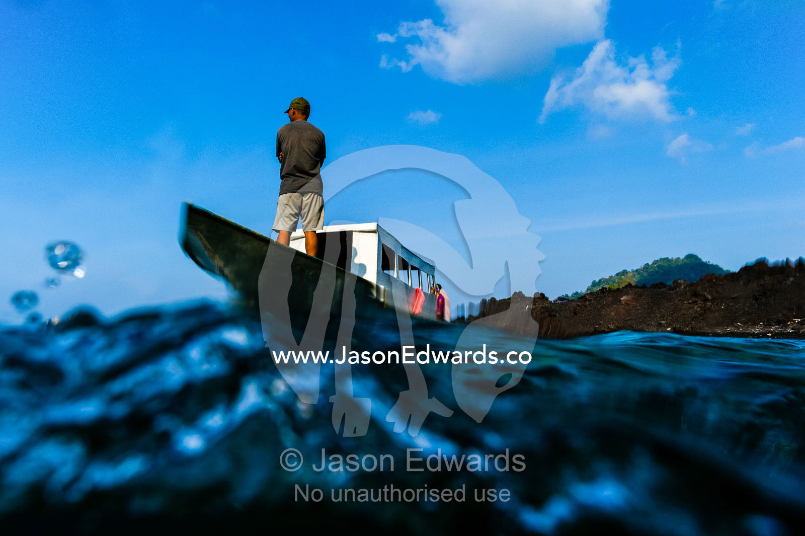 A fisherman standing on the bow of his boat from the water level. Lava Flow, Banda Neira, Banda Islands, Maluku Province, Indonesia.