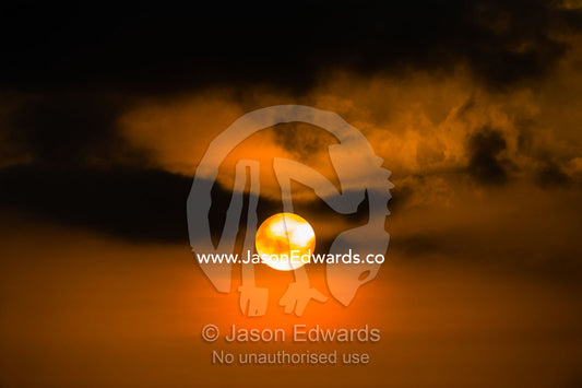 A dark tropical storm cloud passes over the face of the sun. Lava Flow, Banda Neira, Banda Islands, Maluku Province, Indonesia.