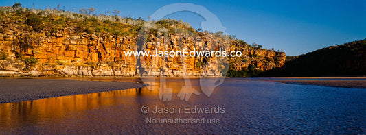 The reflection of orange ochre cliffs in a tidal pool on a beach at sunset. Calamity Bay, Koolama Bay, Kimberley Coast, Western Australia, Australia.