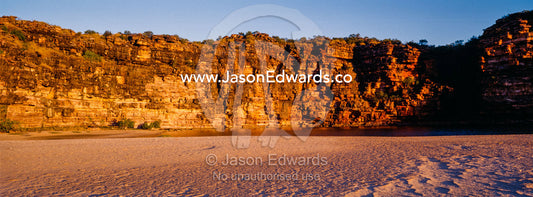 A rugged red sandstone cliff above a deserted beach at sunset. Calamity Bay, Koolama Bay, Kimberley Coast, Western Australia, Australia.
