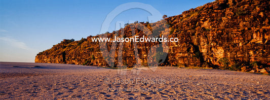 A rugged red sandstone cliff above a deserted beach at sunset. Calamity Bay, Koolama Bay, Kimberley Coast, Western Australia, Australia.