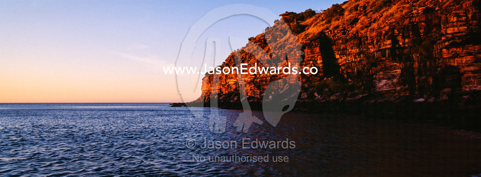A rugged red sandstone cliff above the ocean at sunset. Calamity Bay, Koolama Bay, Kimberley Coast, Western Australia, Australia.
