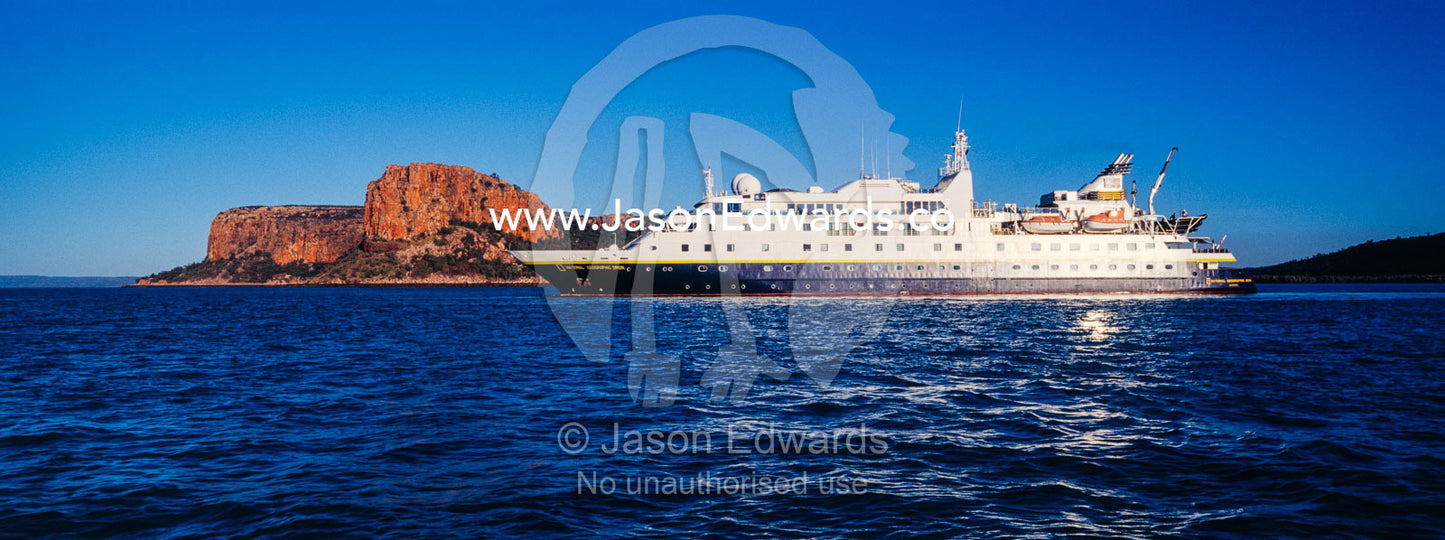 A cruise ship moored near an ochre sandstone headland on a desert coastline. Raft Point, Doubtful Bay, Buccaneer Archipelago, Kimberley Coast, Western Australia, Australia.