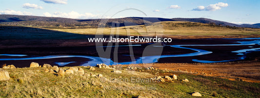 A winding river flows across an alpine plain at sunset. Tantangara Reservoir, Kosciuszko National Park, New South Wales, Australia.