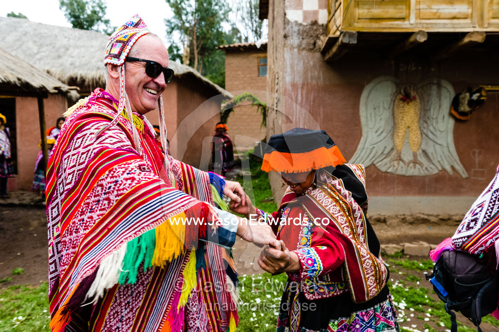 A woman wears a traditional Lliclla dancing with a tourist wearing a poncho and chullo woven hat. Peru.