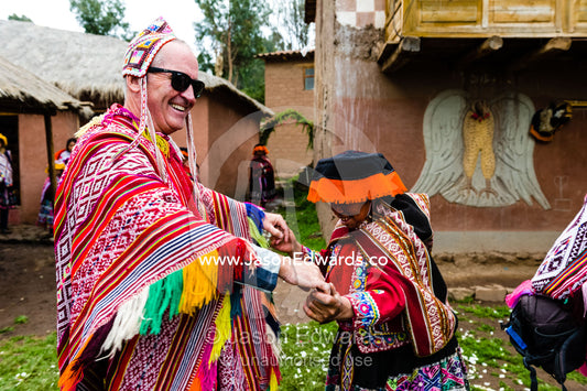 A woman wears a traditional Lliclla dancing with a tourist wearing a poncho and chullo woven hat. Peru.